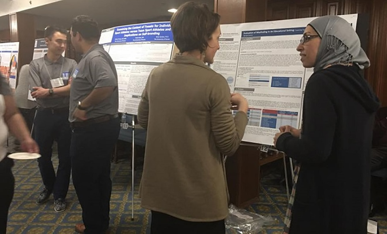 Individuals are conversing at a conference with visual displays in background